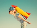 Happy child playing with toy rocket against summer sky background. Retro toned